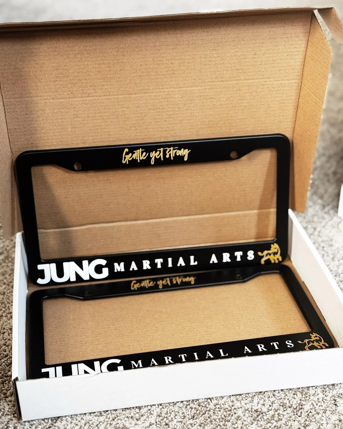 Black and gold Jung Martial Arts custom UV-printed license plate frames packaged for delivery