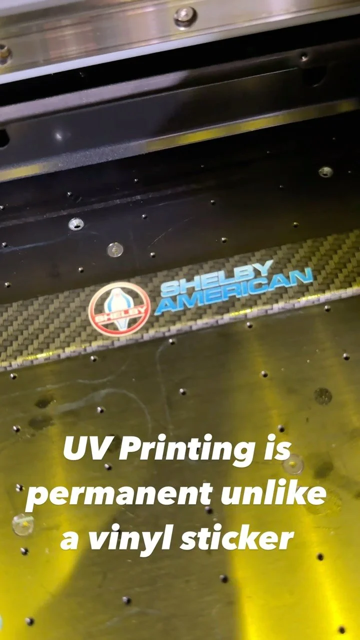 Shelby American logo UV-printed onto a carbon fiber bracket inside a Roland UV flatbed printer